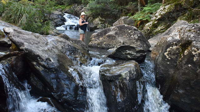 Woman standing in a waterhole with a waterfall in the background and another waterfall in the background, taken of Fiona Greenhill at Booloumba Creek in Conondale National Park, half way to the main Booloumba Creek Falls