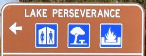 Brown sign for Lake Perseverance, with blue symbols for toilets, picnic area, and fireplace