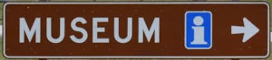 Brown sign for Museum, with a blue and white information centre symbol