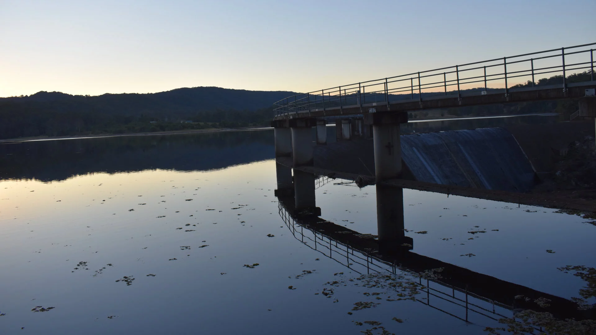 Late afternoon dam surface with mountain hills in the background and curved dam wall to the right, Wappa Dam near Yandina