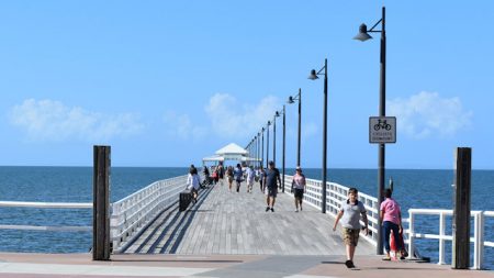 Start of a timber deck pier with wooden handrails and a row of street lamps on one side, taken of Shorncliffe Pier in Brisbane