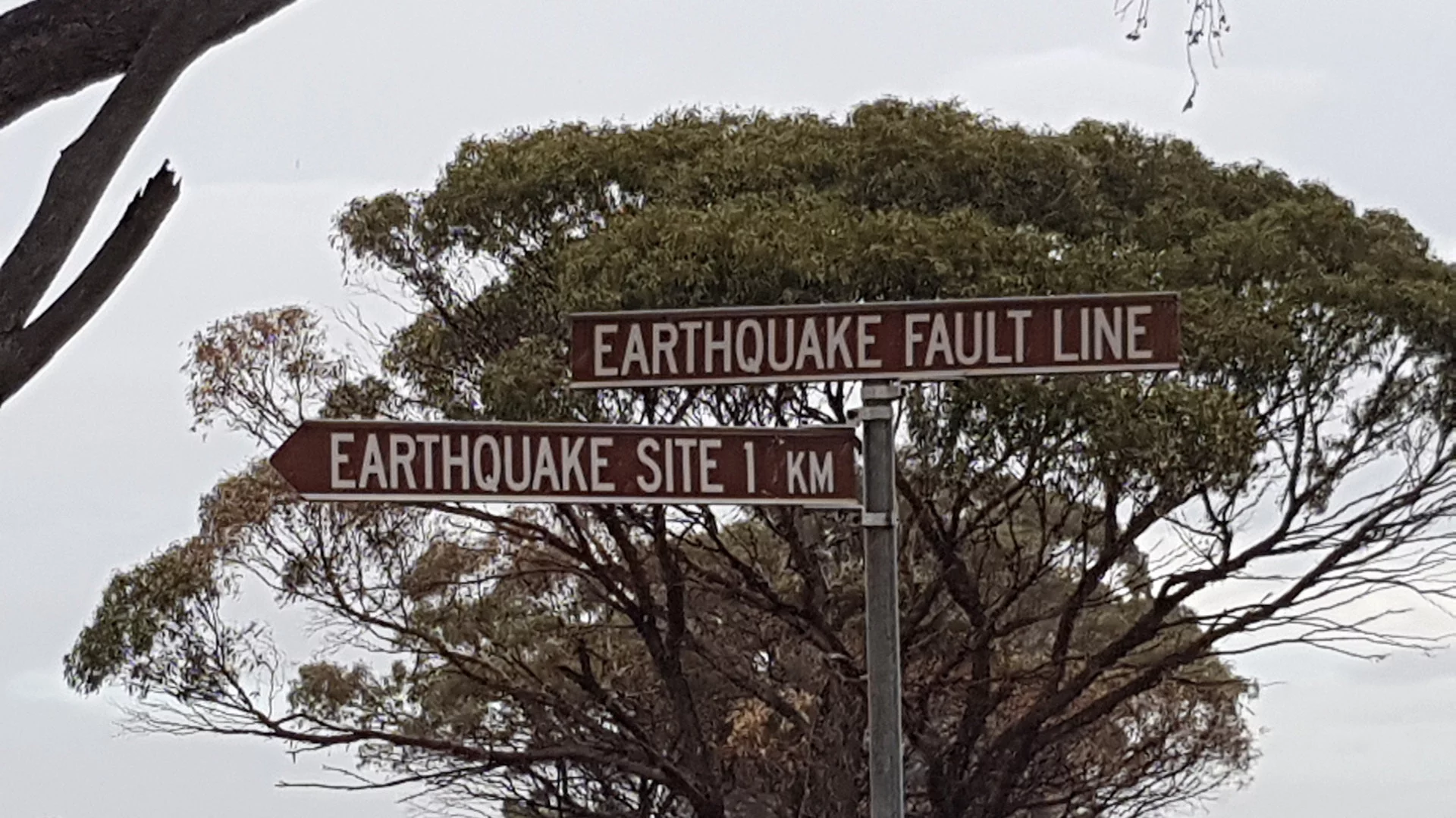 Brown sign of the Earthquake Fault Line taken at the site of where the fault line exists, also showing a brown sign to an Earthquake Site 1km away