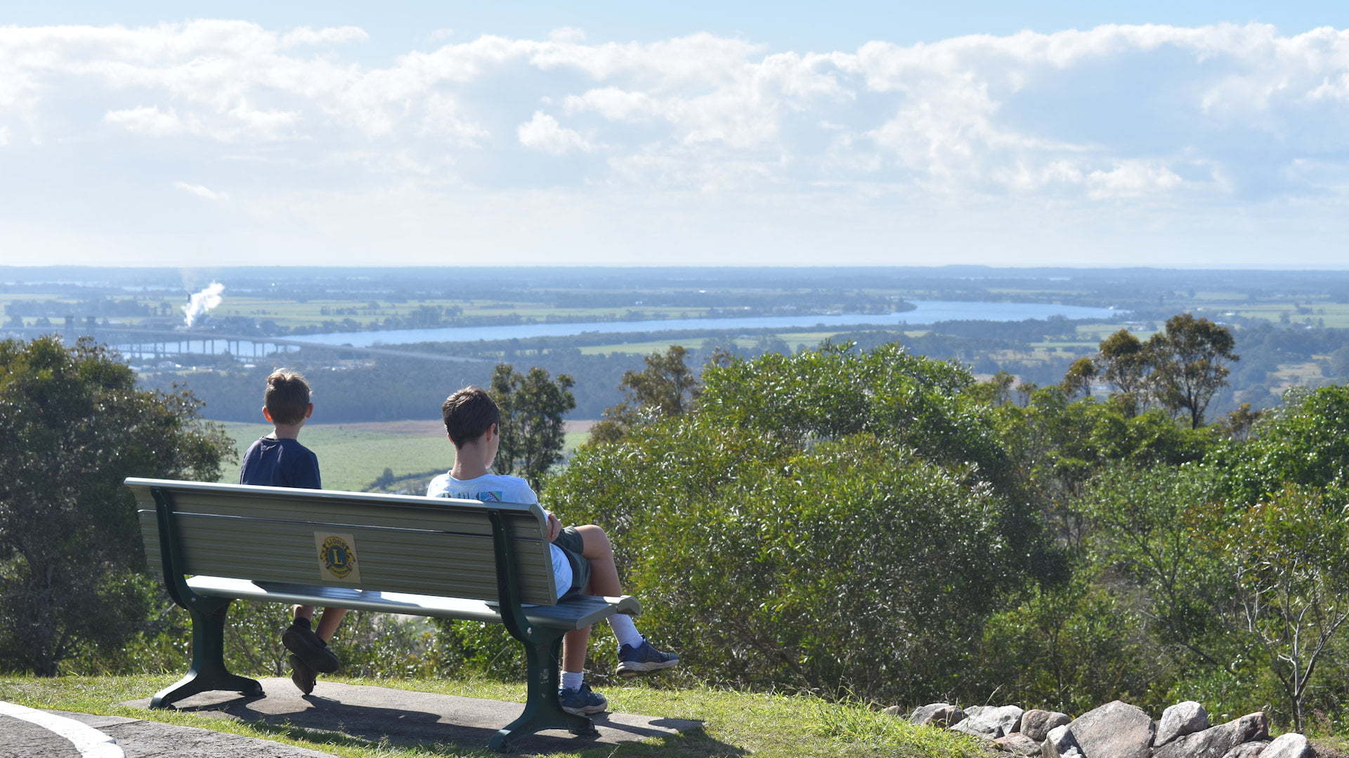 Two boys on a bench seat looking at a view from a lookout, taken at the Maclean Lookout towards the Clarence River and Iluka