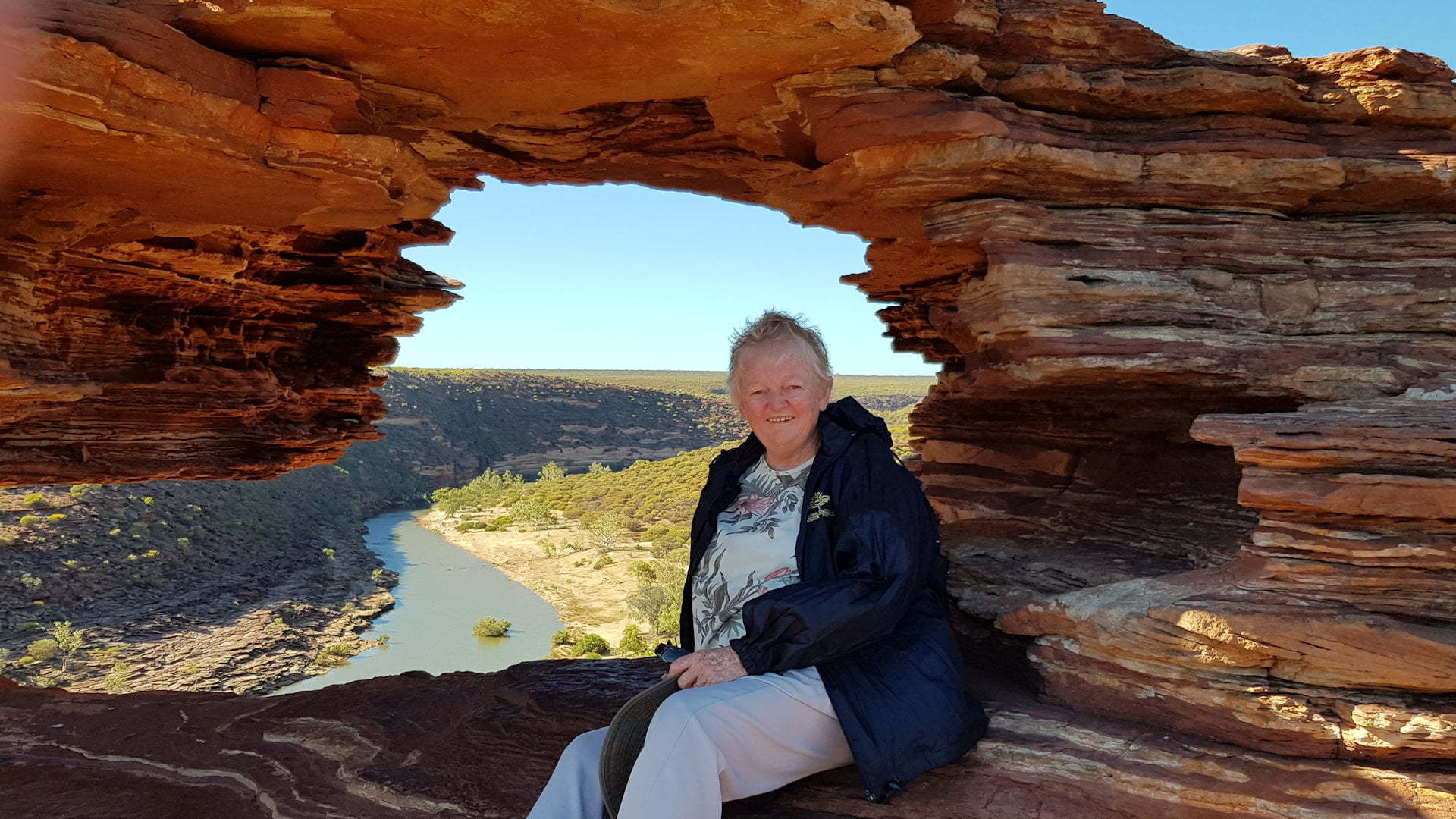 Woman sitting in front of a rock formation called Natures Window with a river in the background