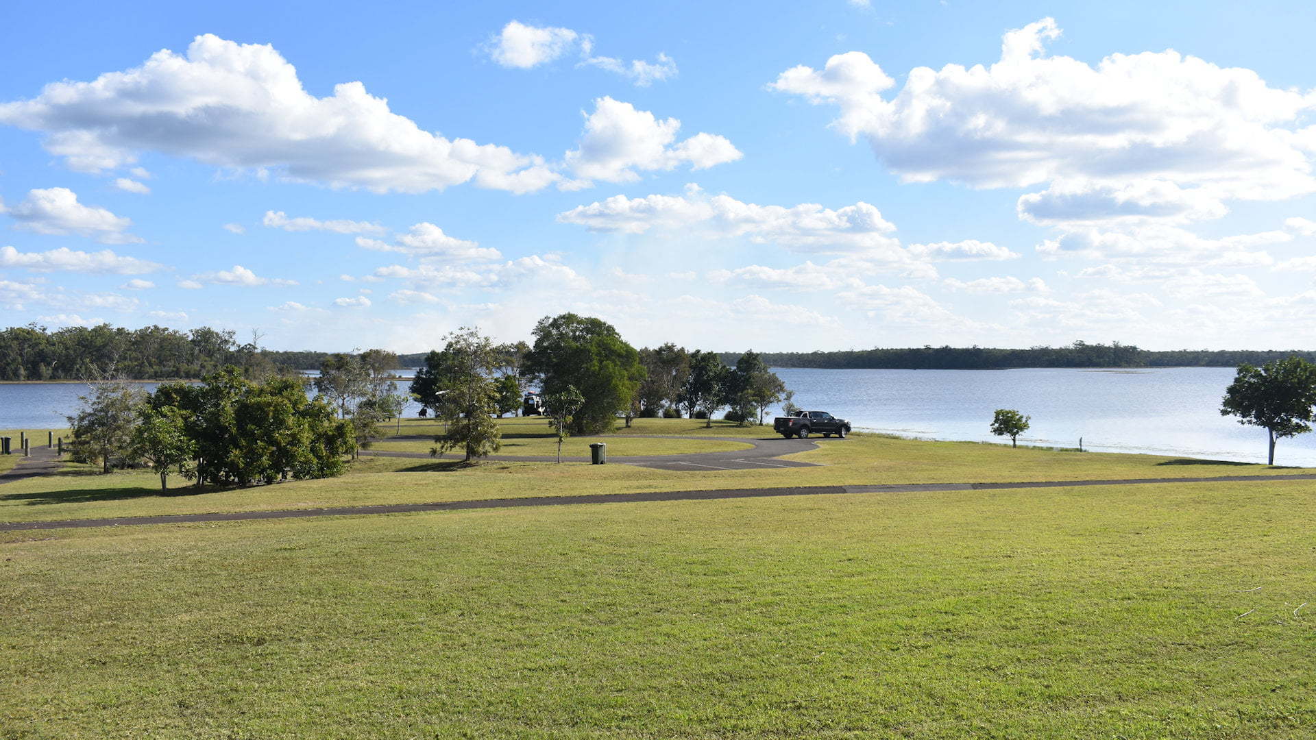 Lake Lenthall camping area, green grass foreground with the lake behind and blue sky with clouds