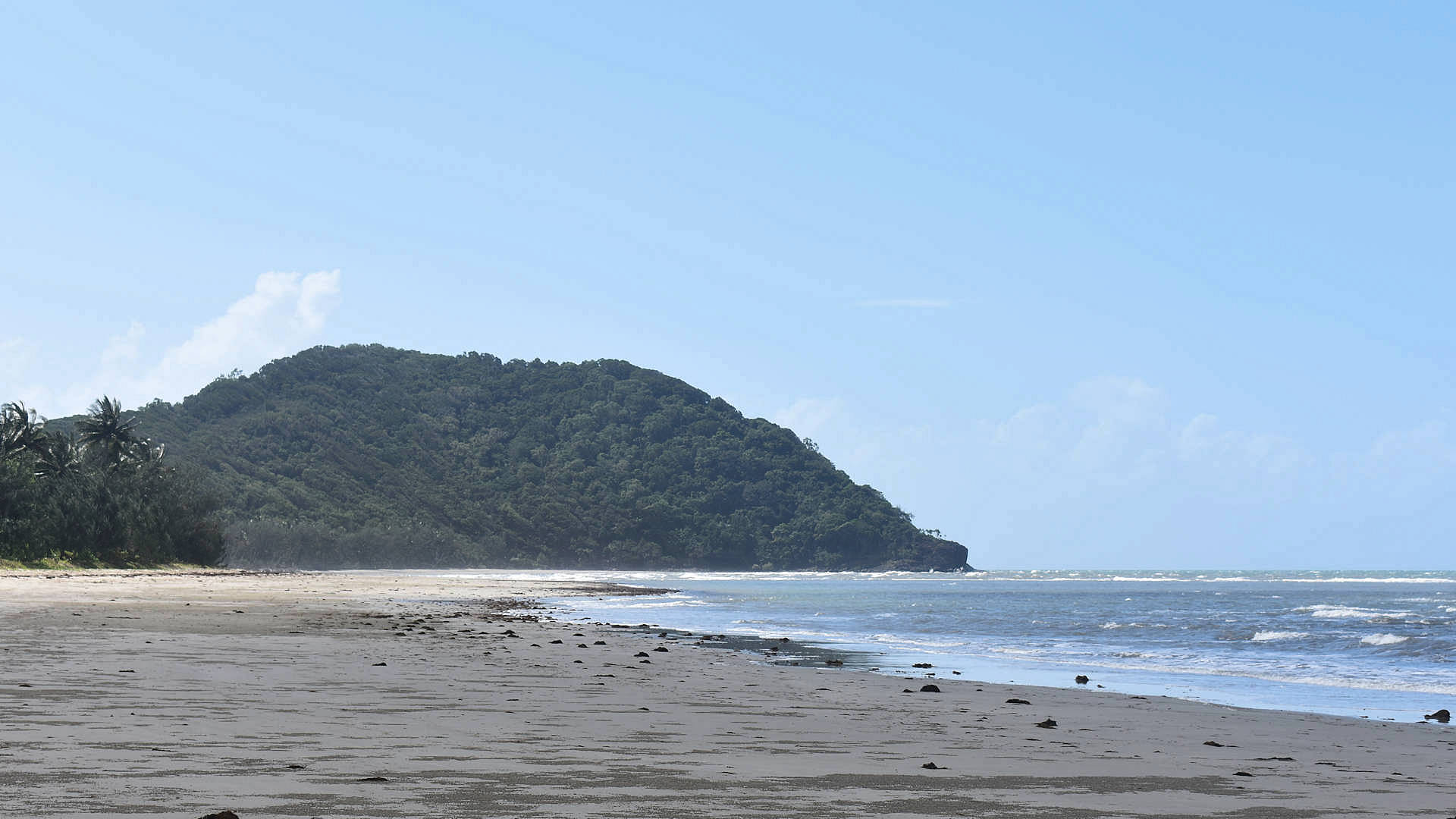 Sandy beach at low tide with blue skies, headlands of Cape Tribulation in the distance, taken at Myall Beach