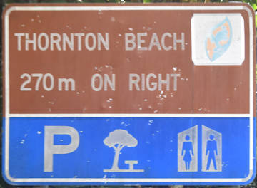 Brown sign for Thornton Beach, 270m on right, blue symbols for Parking, park, and toilets