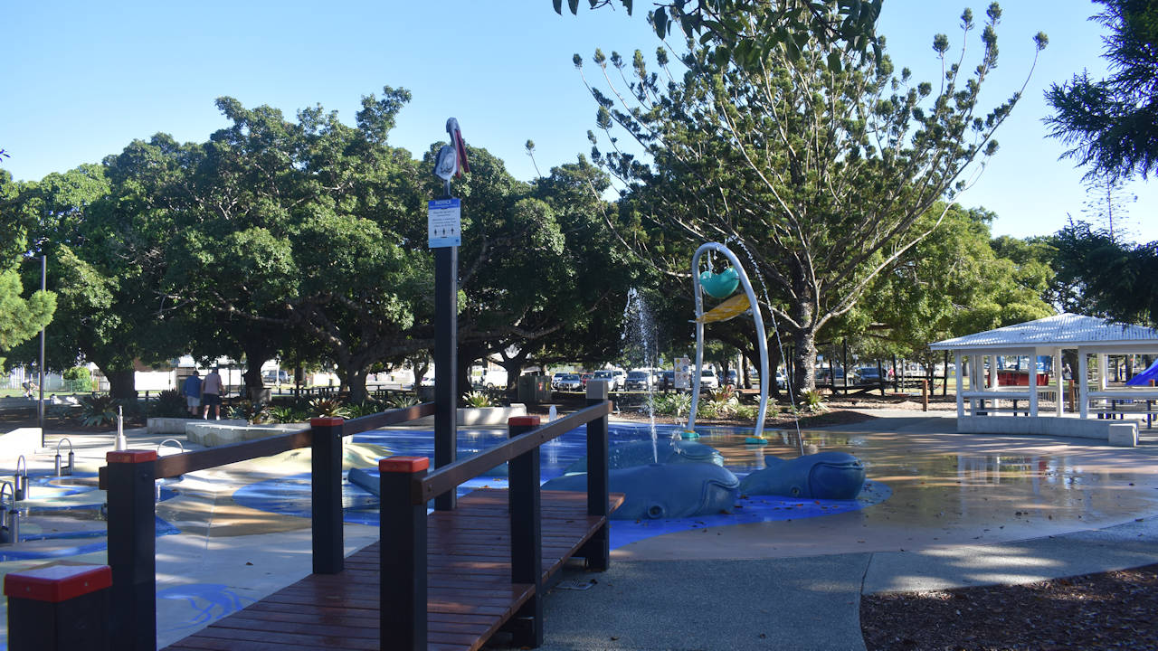 Water playground with whales spurting water, spilling water bucket, wooden bridge in foreground