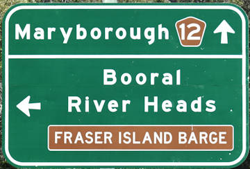Brown sign for Fraser Island Barge, green sign for Booral and River Heads, and Maryborough with Tourist Drive 12 symbol