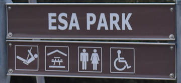 Brown sign for Esa Park, symbols for playground, sheltered picnic tables, toilets, disabled access