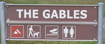 Brown sign for The Gables, symbols for no camping, dogs on leash, boat ramp, toilets